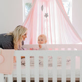 Woman interacting with a baby in a crib with pink bedding and canopy.
