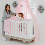 Woman and child in a crib with pink canopy and decorative elements.