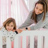 Woman and child in a crib with pink and white bedding