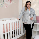 Woman standing next to Jazz Cot / Co-Sleeper in a nursery with floral decorations on the wall.