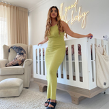 Aisha Baker in a neon green dress standing in a nursery with a crib and 'Good old baby' sign.